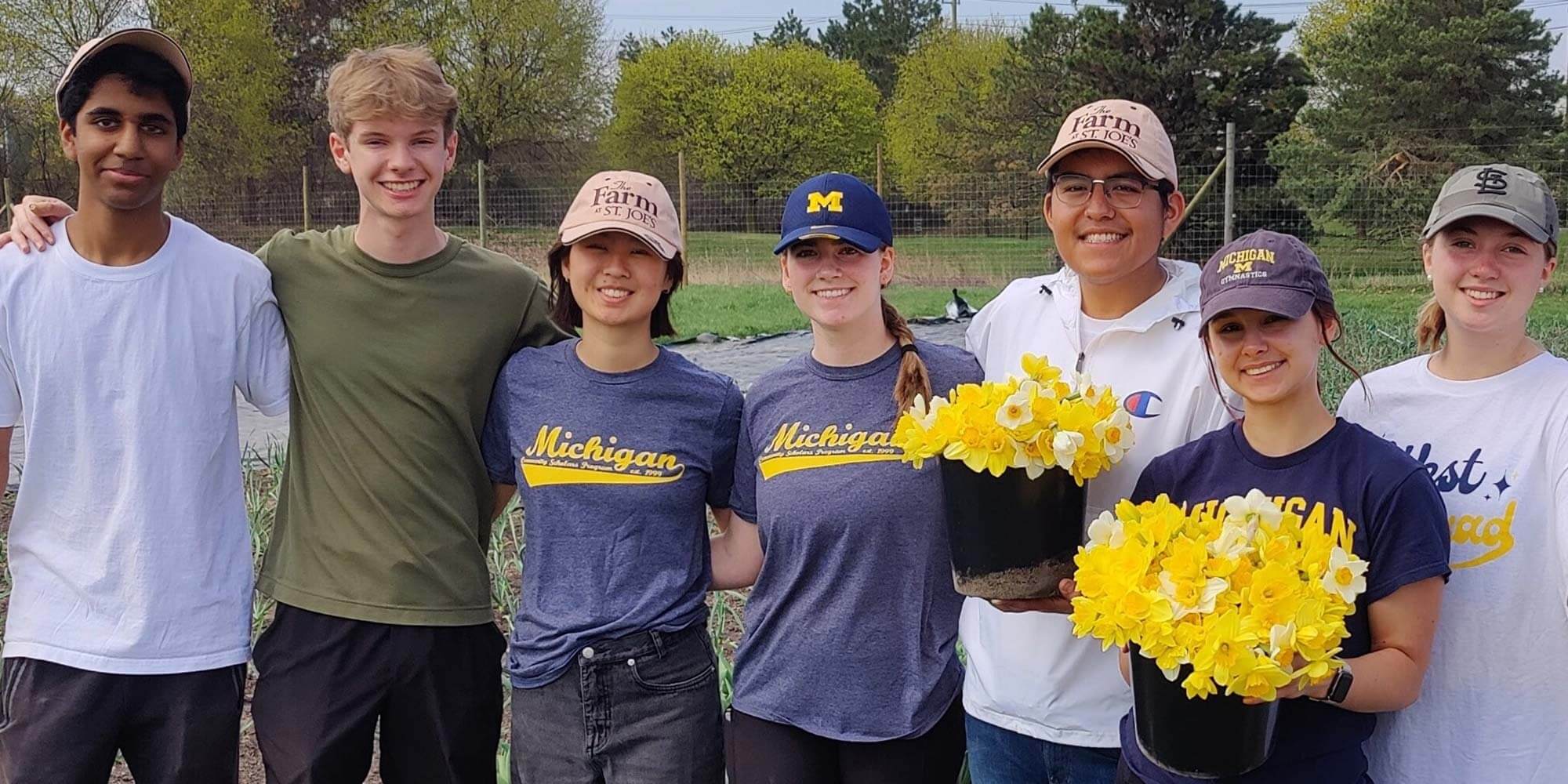 A group of high school or college-aged students lock arms as they volunteer at The Farm. Most are wearing University of Michigan clothing.