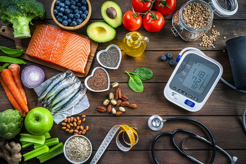 Colorful foods surrounding a blood pressure meter, stethoscope and measuring tape.