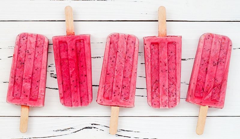 Three berry popsicles laid out on a white wood table.