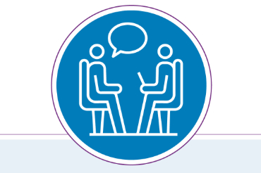 Icon of two people sitting across a table, one with a laptop, and a speech bubble between them, indicating a conversation or interview.