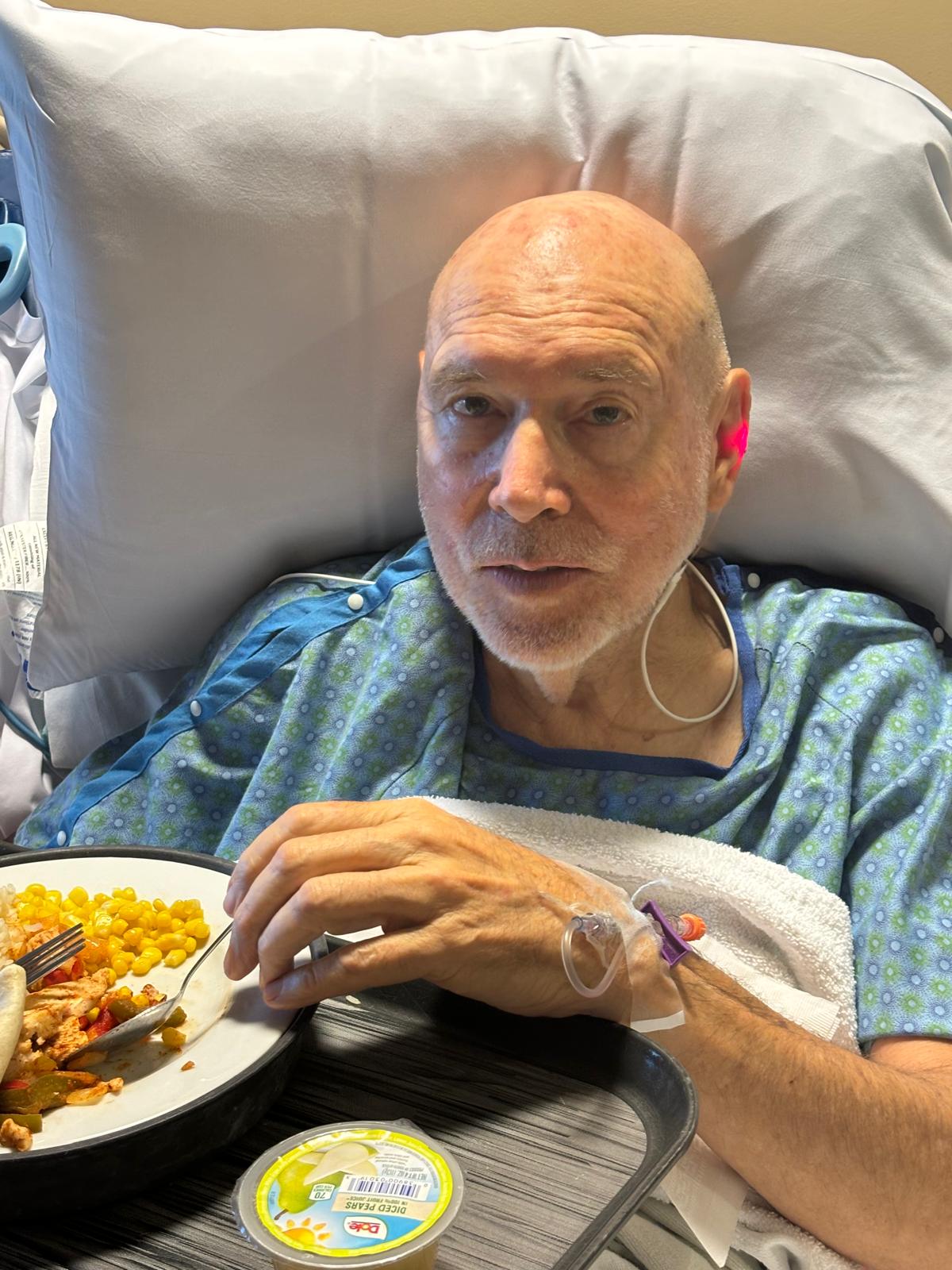Bob in hospital bed with a meal after his stroke