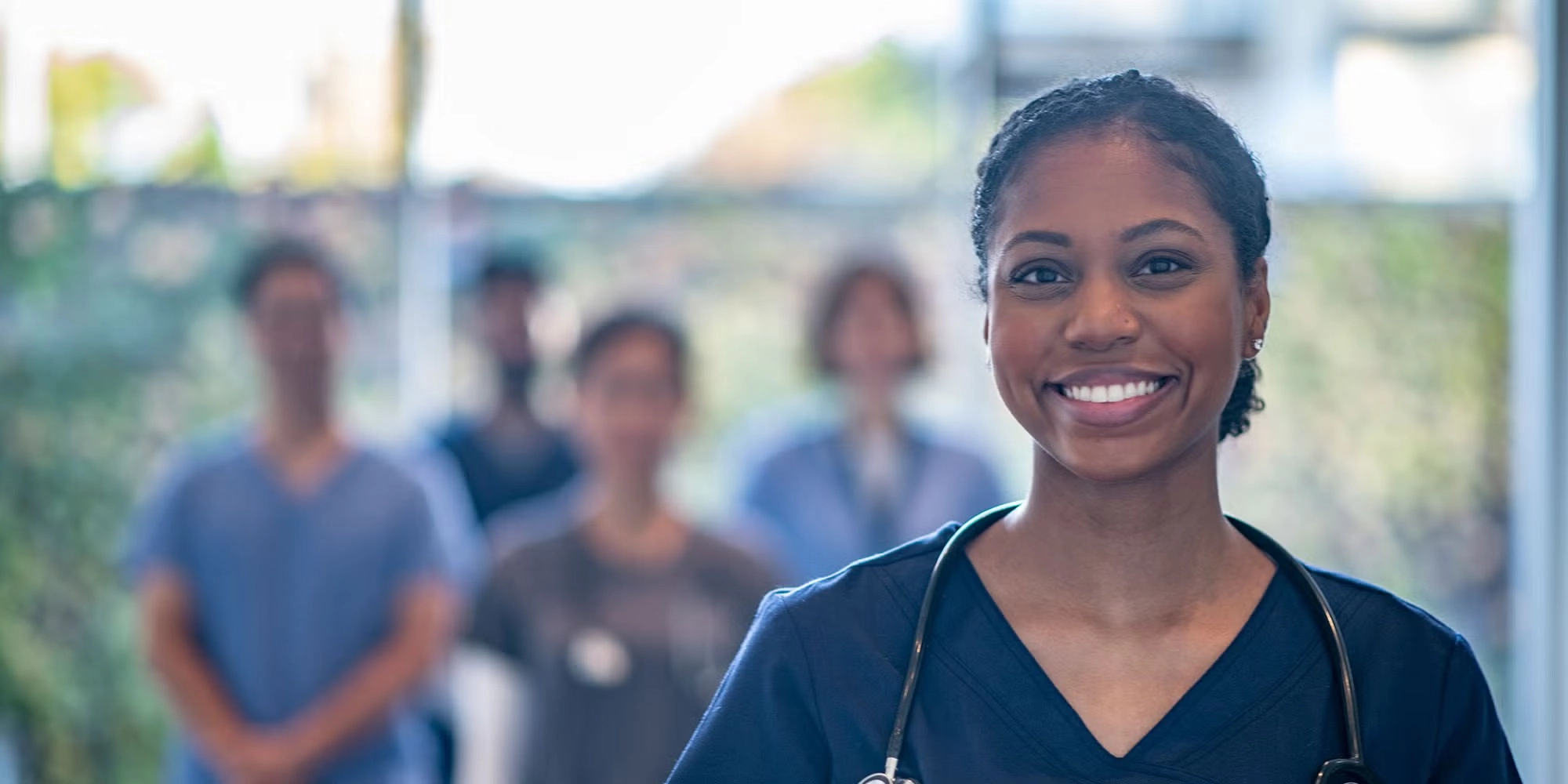 A group of medical residents in scrubs stand in a hallway. One woman is closer than the rest and she's smiling at the camera.