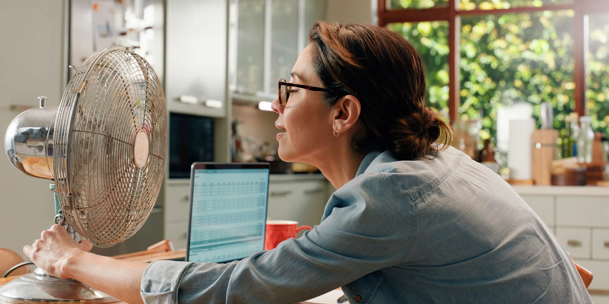 A woman cools off during a hot flash using a table fan in her kitchen